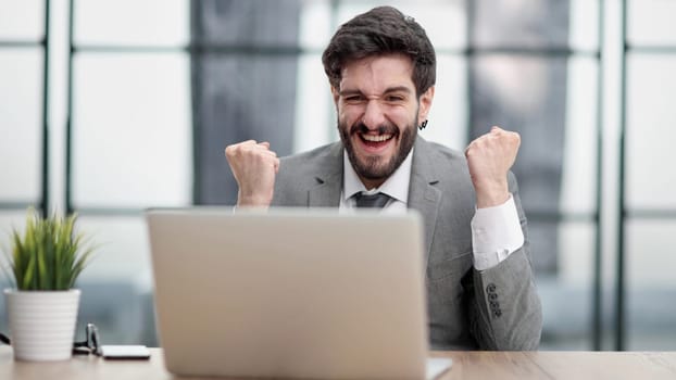 Excited businessman sitting at table with laptop and celebrating success