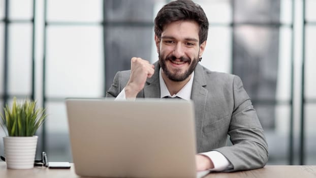 Excited businessman sitting at table with laptop and celebrating success