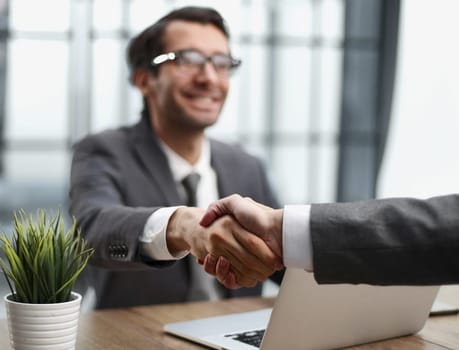 Two positive confident businessmen shaking hands over meeting table after negotiation,