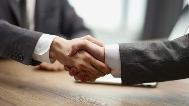 shaking hand of crop male colleague over table while greeting and introducing in office