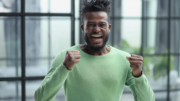 human emotions, reactions and feelings. Joyful young black man clenching his fists expressing joy and success,