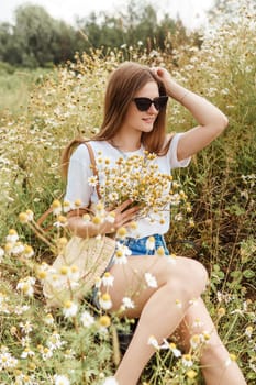 Beautiful young woman in nature with a bouquet of daisies. Field daisies, field of flowers. Summer tender photo.