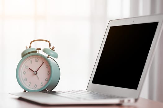 An alarm clock with a computer laptop on the table for the concept of work, study and time management.