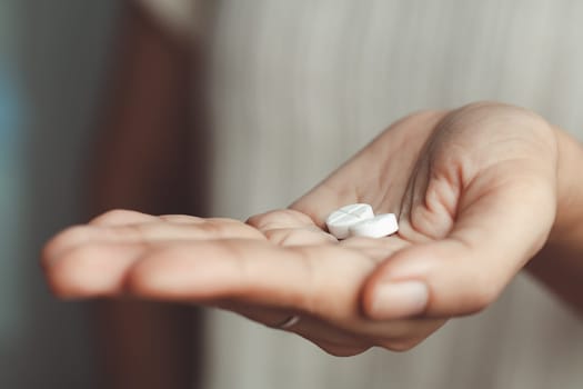 Two white pills on asian woman's hand for medical and healthcare concept.