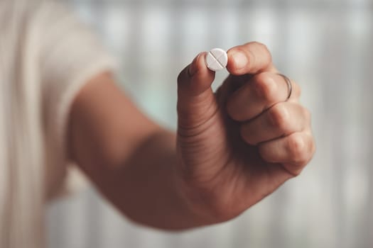 Asian woman's hand holding a white pill for medical and healthcare concept.