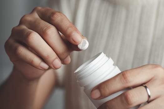 Asian woman's hand taking medicine from a white bottle for medical and healthcare concept.