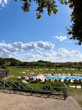 Swimming pool with sun loungers under sun umbrellas on a green meadow. Villa Cordevigo. Verona, Italy. High quality photo