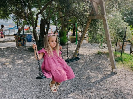 Little girl swings on a chain swing in the park among the trees. High quality photo