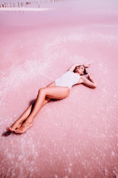 Woman in a pink salt lake. She lies in a white bathing suit. Wanderlust photo for memory.