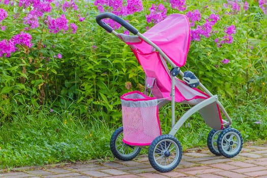 Baby pink stroller forgotten in a city park. The child lost the pram. Toy carriage for dolls in a public park. Girl games in the fresh air.