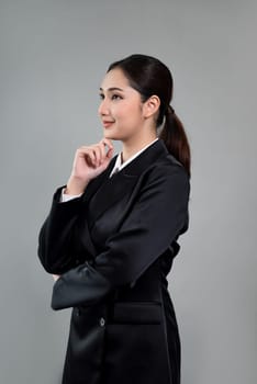 Confident young businesswoman stands on isolated background, posing in formal black suit. Office lady or manager with smart and professional appearance. Enthusiastic