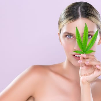 Alluring beautiful woman model portrait holding green leaf as concept for cannabis skincare cosmetic product for perfect skin freshness treatment in isolated pink background.