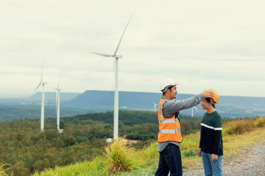 Engineer with his son on a wind farm atop a hill or mountain in the rural. Progressive ideal for the future production of renewable, sustainable energy. Energy generation from wind turbine.