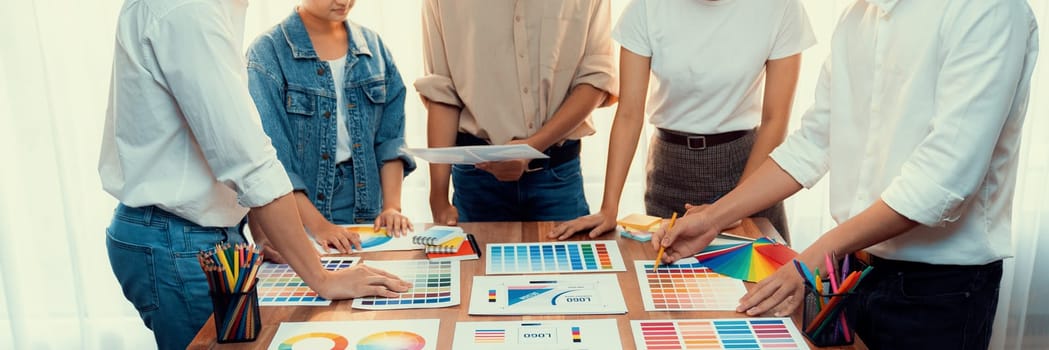 Graphic designer brainstorm logo and graphic art at busy creative studio workshop. Experiment and brainstorm color palette and pattern at workspace table for creative design. Panorama shot. Scrutinize