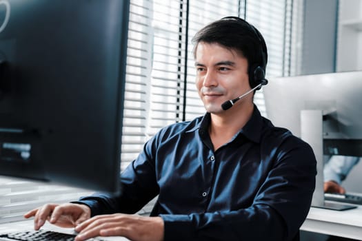 Young competent asian male call center agent working at his computer while simultaneously speaking with customers. Concept of an operator, customer service agent working in the office with headset.