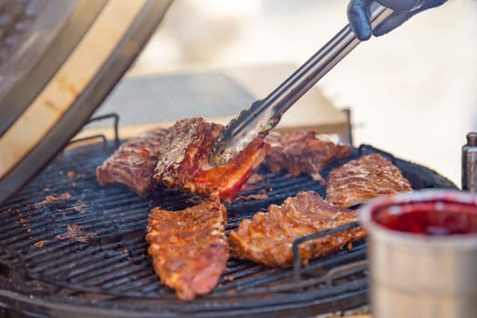 The process of grilling ribs. A man turns a piece of grilled ribs with tongs while grilling meat. This is the season for barbecues and outdoor cooking. High quality photo