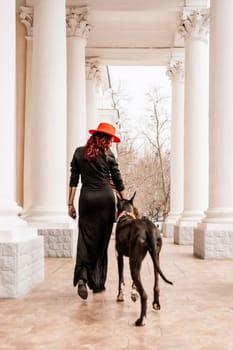 A photo of a woman and her Great Dane walking through a town, taking in the sights and sounds of the urban environment.