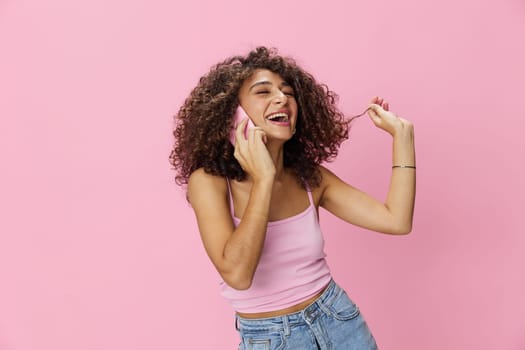 Woman with curly afro hair talking in pink top and jeans on pink background, smile, happiness, copy space. High quality photo