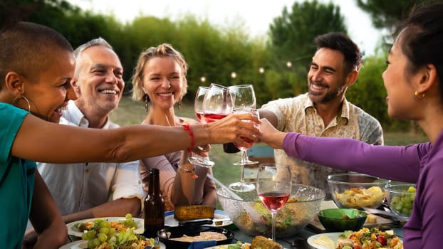 Happy middle age friends toasting with wine during barbecue garden dinner party in the evening. Lifestyle. Panoramic horizontal image.
