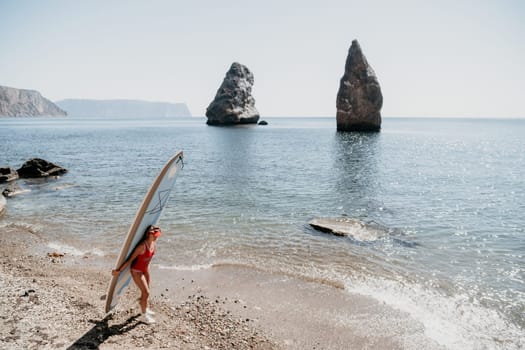 Close up shot of beautiful young caucasian woman with black hair and freckles looking at camera and smiling. Cute woman portrait in a pink bikini posing on a volcanic rock high above the sea