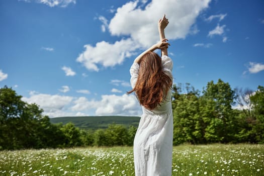 a woman stands with her back to the camera in a light dress in a chamomile field with her hands raised above her head. High quality photo