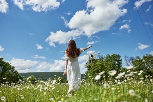 a woman in a long light dress stands in a chamomile field and holds out her hand to a clear, clear sky. High quality photo