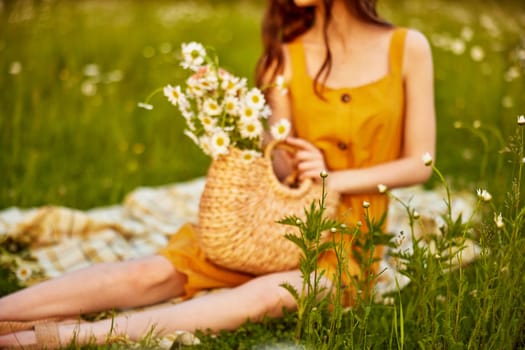 a girl in an orange dress and sandals sits in a chamomile field with a wicker basket full of flowers. High quality photo