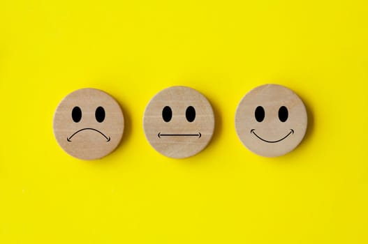 Happy, sad and neutral emoticon faces on wooden circle with yellow background cover. Customer feedback, satisfaction and evaluation and concept.