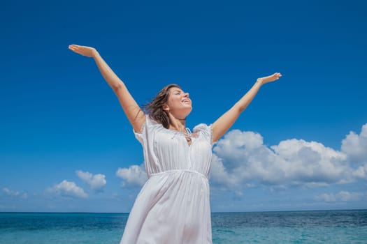 Beautiful young woman in dress on beach with hands raised