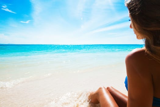 Happy tanned girl in bikini at seaside, blue sea water in background