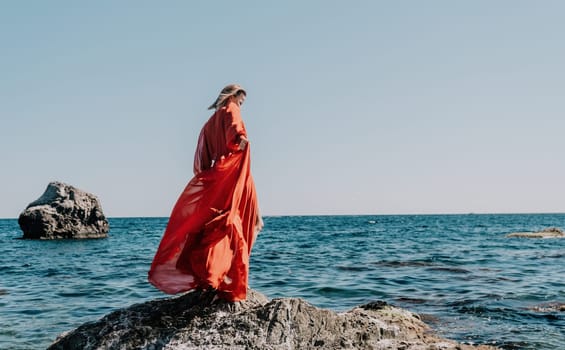 Woman travel sea. Young Happy woman in a long red dress posing on a beach near the sea on background of volcanic rocks, like in Iceland, sharing travel adventure journey