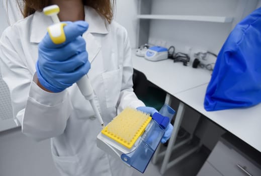 A young female scientist works in a sterile genetic or bacteriological laboratory with a dispenser and reagents in a medical gown, gloves and a doctor's cap.
