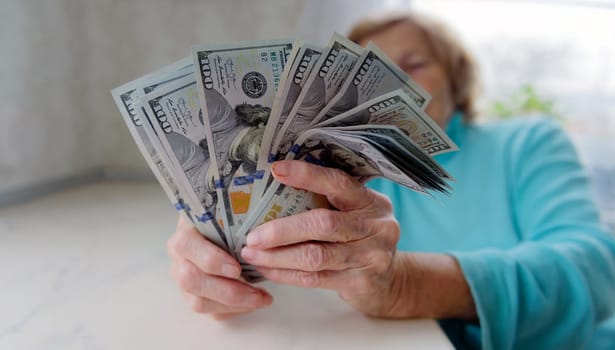 Close-up of an elderly woman's hands holding money in 100 dollar bills, compensation.