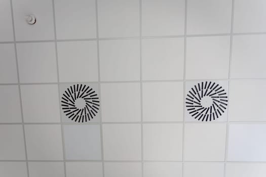 View from below of the system suspended ceiling made of square panels and the ventilation placed in it. New trend of lowering ceilings