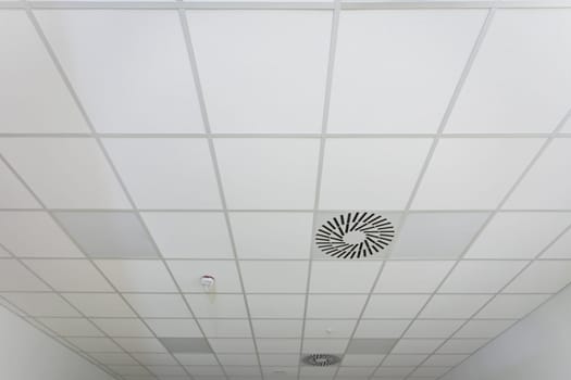 View from below of a large plane of suspended panel ceiling made in a narrow room.