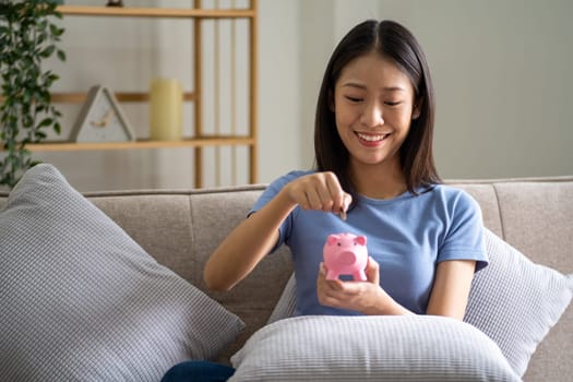 Young smart Asian teenager putting coin in a piggy bank, happy young woman who puts coin in piggy bank for saving, investment economical. High quality photo