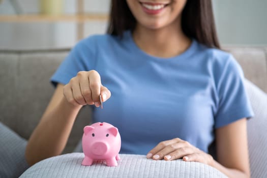Young smart Asian teenager putting coin in a piggy bank, happy young woman who puts coin in piggy bank for saving, investment economical. High quality photo