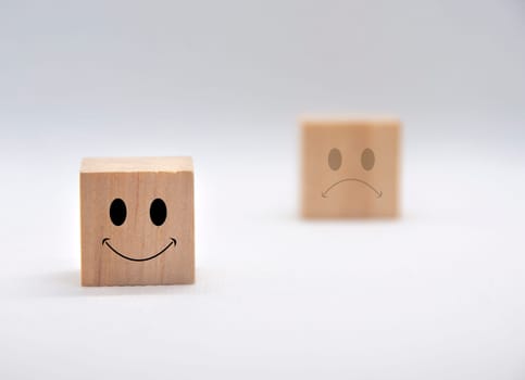Happy and sad emoticon faces on wooden cubes with white background cover. Customer feedback, satisfaction and evaluation concept.