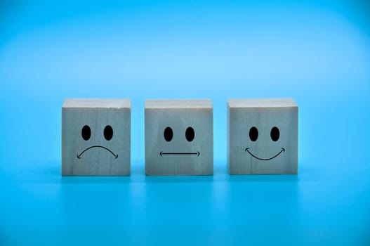 Sad, neutral and happy emoticon faces on wooden cubes with blue background cover. Customer satisfaction and evaluation concept