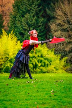 Young beautiful woman in circus costume play with red fans in the park.