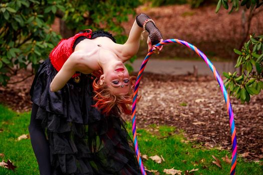 Young beautiful woman in circus costume play with hula hoop in the park.