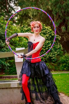 Young beautiful woman in circus costume play with hula hoop in the park.