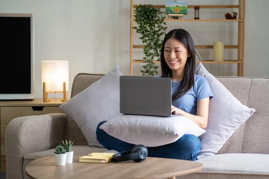 Happy cheerful young asian woman sitting on sofa with laptop, smart beautiful young asian woman chilling in house with laptop. High quality photo