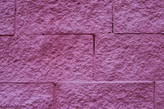 A fragment of a wall made of stone bricks painted in dark pink, red.