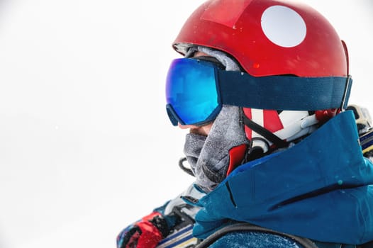 A sportsman in a helmet and goggles in profile against the background of white falling snow, looks to the side enjoying a beautiful view of the mountains.