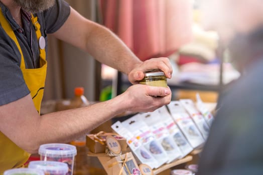 The seller in the confectionery shop opens a jar of jam and shows it to the customer. Male hands open a jar of fruit jam. High quality photo