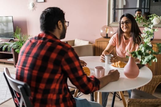 Young diverse loving couple eating croissant and talks together at home in breakfast time. Communication and relationship