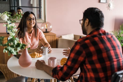 Young diverse loving couple eating croissant and talks together at home in breakfast time. Communication and relationship