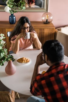 Young diverse loving couple eating croissant and talks together at home in breakfast time. Communication and relationship