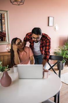 technology, remote job and lifestyle concept - happy indian man in glasses with laptop computer working at home office